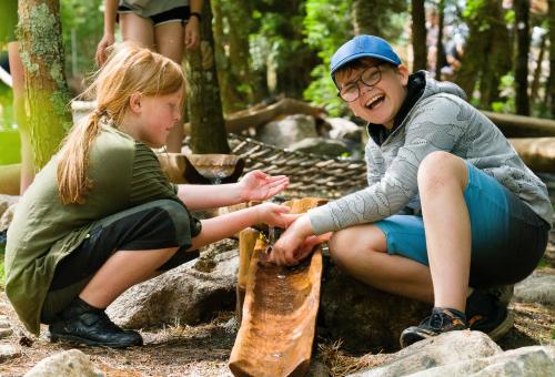 Boy and girl playing with water coming down a bamboo gutter into a pool